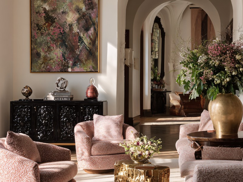 Individuell gestaltetes Altbau-Wohnzimmer mit rosa Sesseln, Gemälde, opulentem Blumenstrauß und antiker Kommode